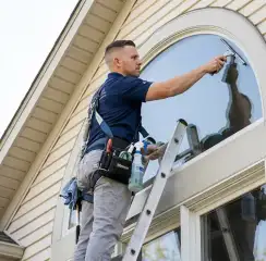 Professional window cleaner on a ladder using a squeegee to clean an exterior arched window, Tacoma, WA.